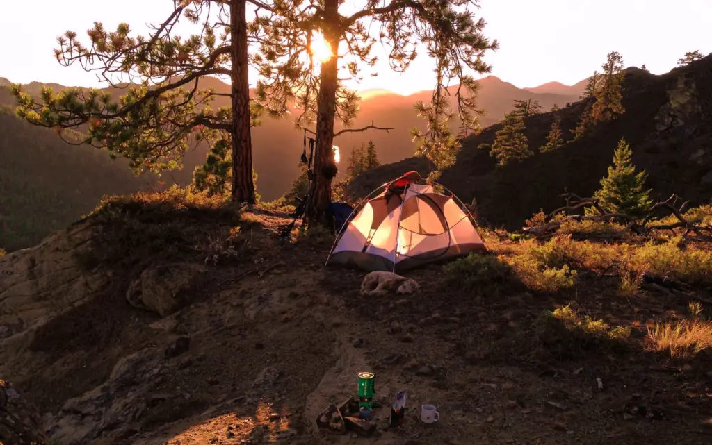 山林中一頂帳篷，遠處可見晨光與山景。